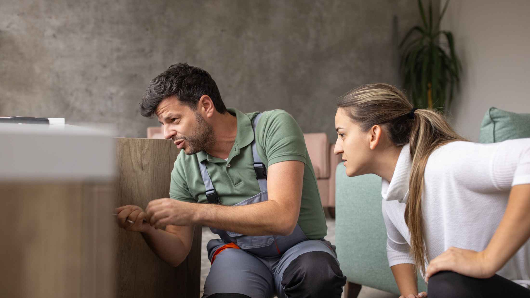 A plumber talking to his client while inspecting a broken sink in her apartment