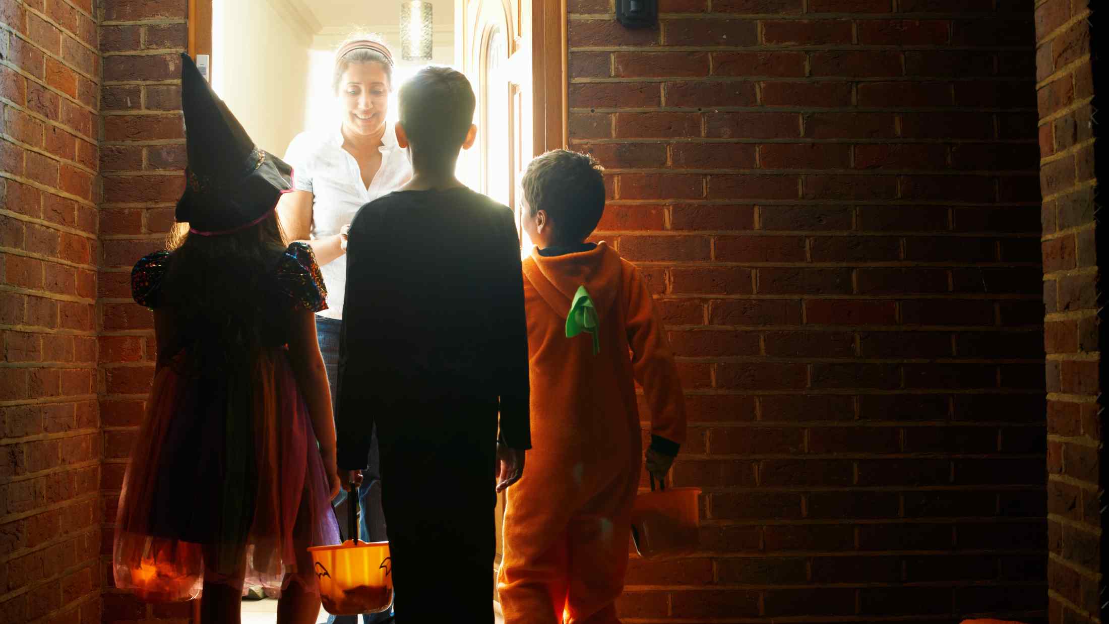 Kids Trick-or-Treating at Door in Halloween Costumes with Candy Buckets